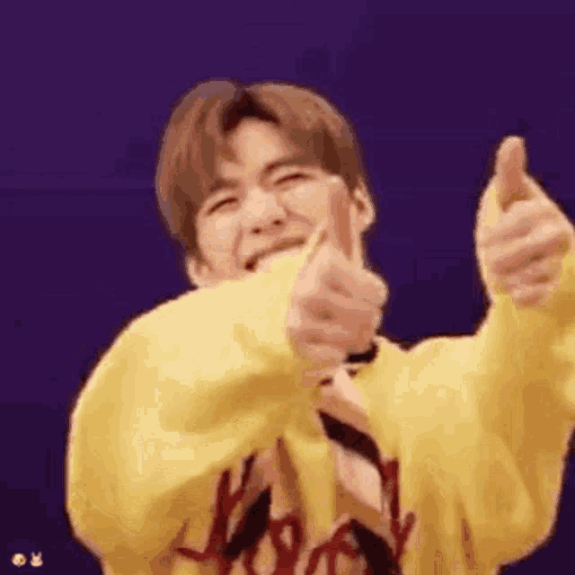a man in a yellow sweatshirt is giving a thumbs up .