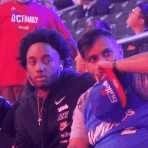 two men are sitting in the stands at a basketball game .