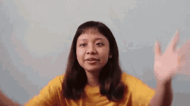 a woman in a yellow t-shirt is waving her hand in front of a blue wall .