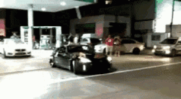a car is driving down a street in front of a gas station at night .