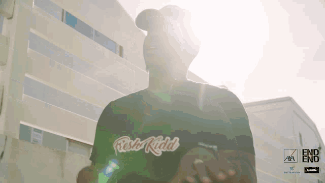 a man wearing a black retro kidd shirt stands in front of a building