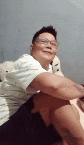 a man wearing glasses and a white shirt is sitting on a bed