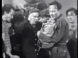 a man is holding a baby in his arms in front of a crowd of people .