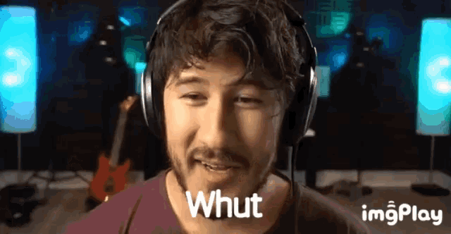 a man wearing headphones says " whut " in front of a guitar