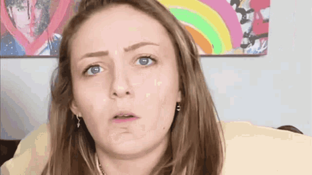 a woman is making a funny face in front of a picture of a rainbow