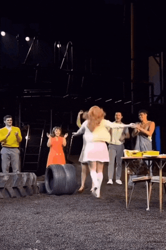 a group of people are standing on a stage applauding a woman in a white dress
