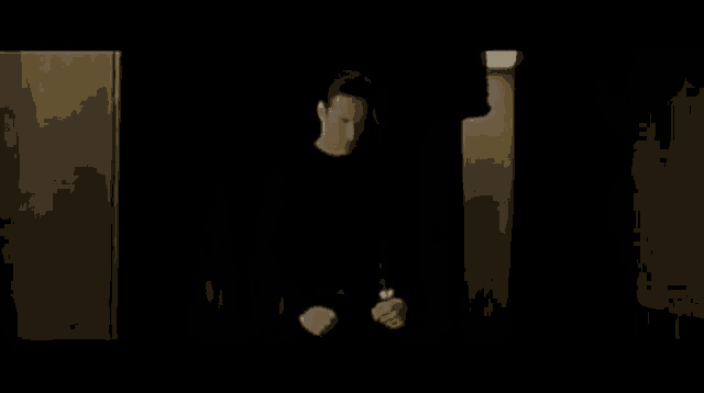 a man in a black shirt is standing in a dark room in front of a window .