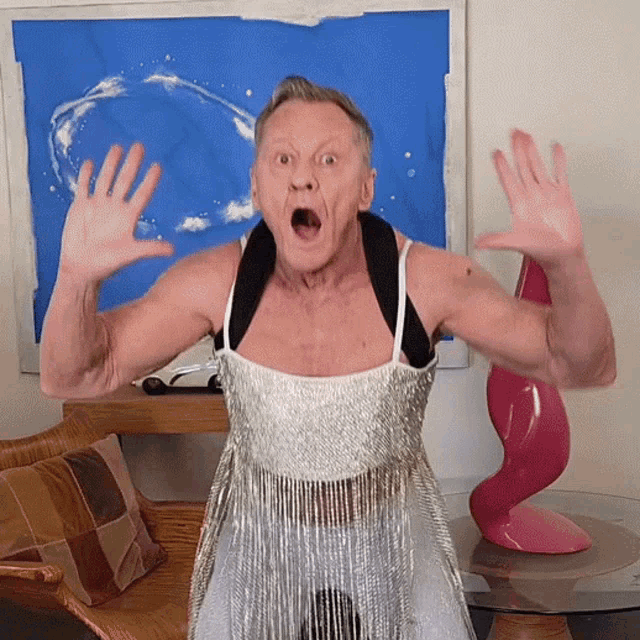a man in a silver dress with fringe is making a surprised face