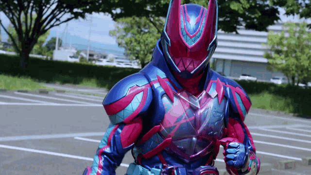 a red and blue superhero is standing in a parking lot with his fist in the air .