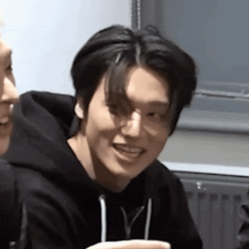 a young man wearing a black hoodie is smiling while sitting next to another man .