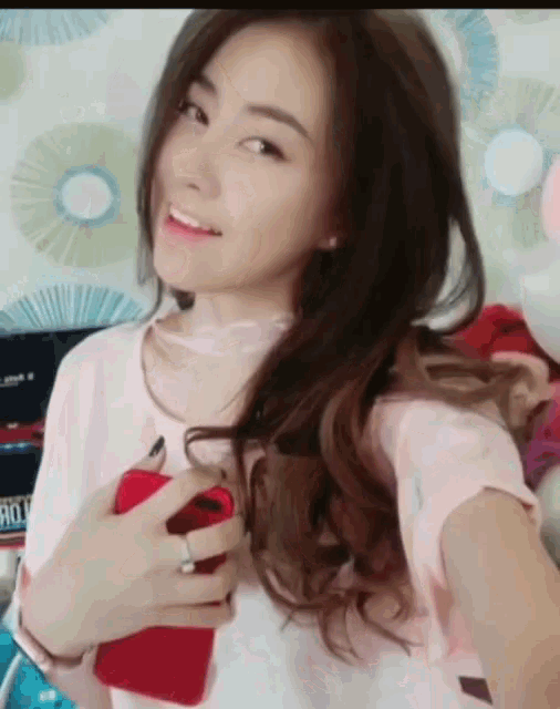 a woman in a pink shirt is holding a red cell phone and smiling