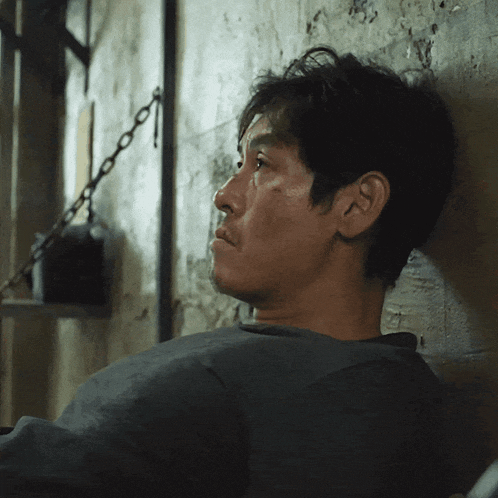 a man leans against a wall with a chain hanging from it