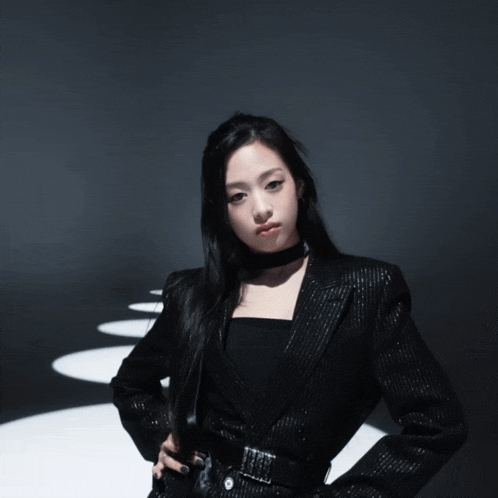 a woman wearing a black jacket and a black choker looks at the camera