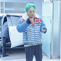 a man with green hair and a striped jacket is standing in front of a car