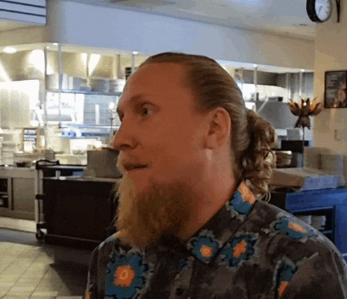 a man with a ponytail and a beard wears a shirt with flowers on it
