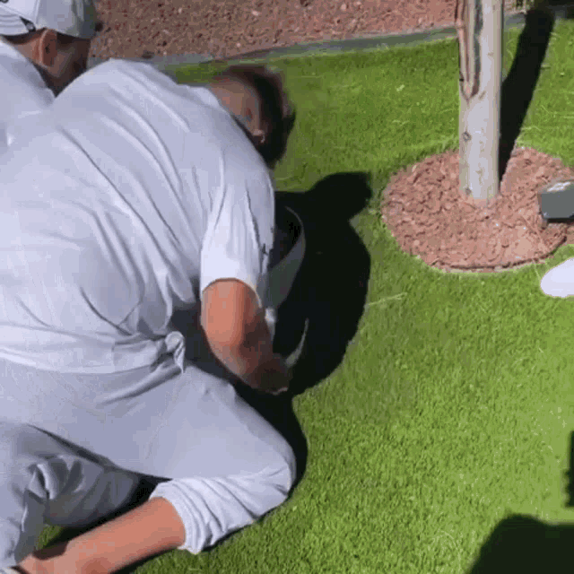 a man is kneeling down on the grass with a bucket in his mouth .