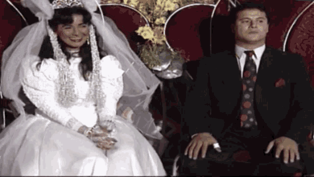 a man in a suit sits next to a bride in a wedding dress