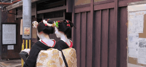 two geishas are walking in front of a building with a no smoking sign