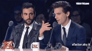 two men are sitting at a table with microphones and a mug with the letter x on it