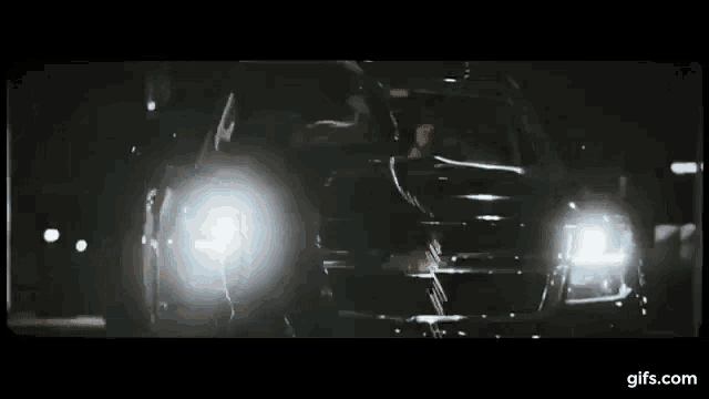 a car is driving down a street at night and the headlights are shining brightly .