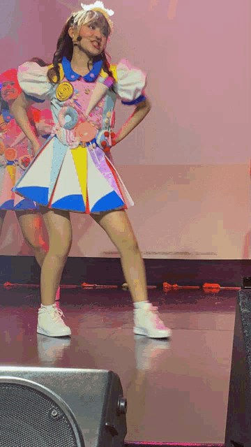 a girl in a colorful dress stands on a stage with her hands on her hips