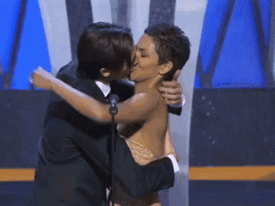 a man in a suit kisses a woman without a shirt on