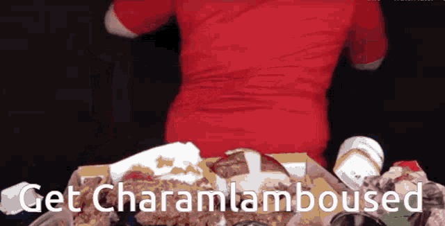 a man in a red shirt is sitting at a table with a bunch of food and the words get charamlamboused