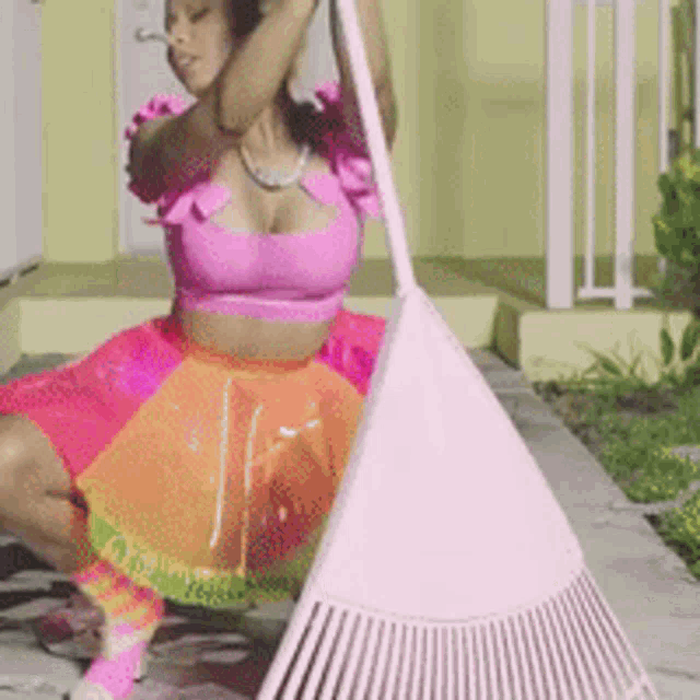 a woman in a pink top and orange skirt is sweeping the floor with a pink rake