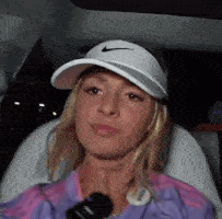 a woman wearing a nike hat and visor is sitting in a car with a microphone .