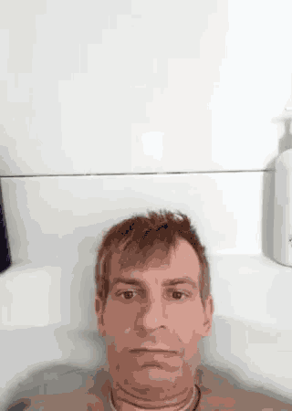 a man is laying in a bathtub with a bottle of shampoo behind him