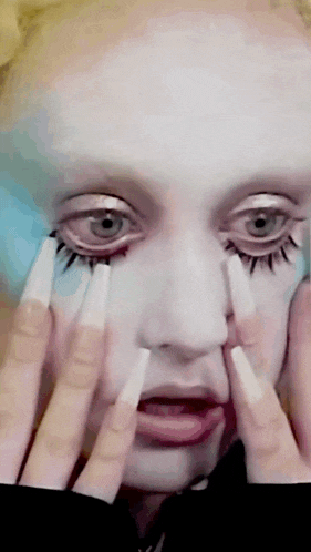 a close up of a woman 's face with long nails and white makeup