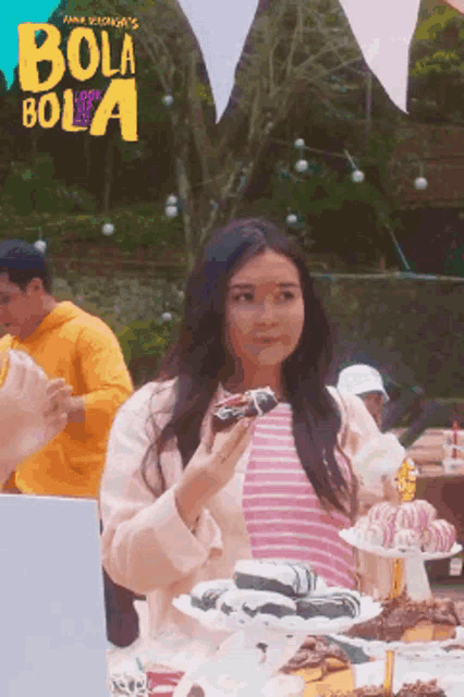 a woman eating a donut in front of a sign that says " bola bola "