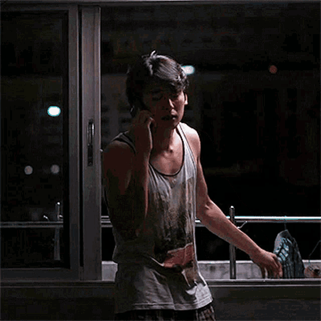 a man wearing a tank top with a palm tree on it is talking on a cell phone
