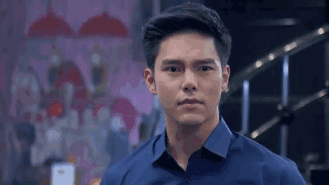a man in a blue shirt is standing in front of a pink wall and looking at the camera .