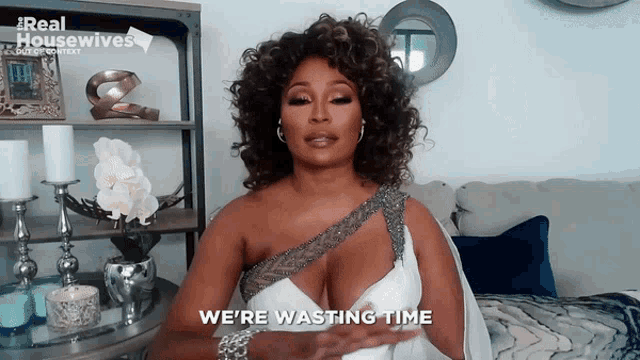 a woman in a white dress says " we 're wasting time " in front of a real housewives sign