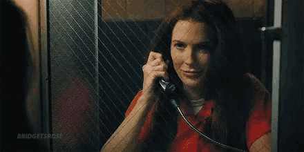 a woman in a jail cell is talking on a phone behind a glass wall .