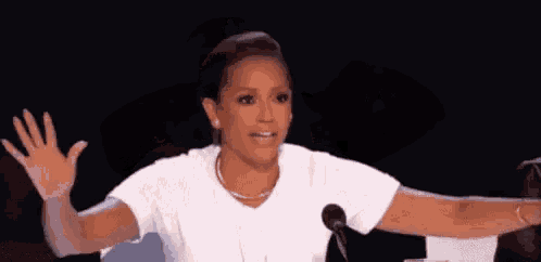 a woman in a white shirt is sitting in front of a microphone with her arms outstretched .