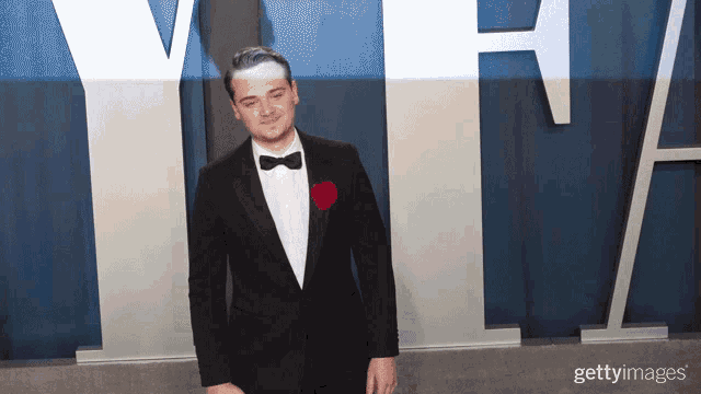a man in a tuxedo and bow tie is standing in front of a large vhh sign