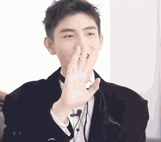 a man in a tuxedo covering his mouth with his hand while wearing a black jacket