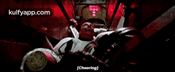 a man is laying in a dark room with a red light behind him and the words cheering .