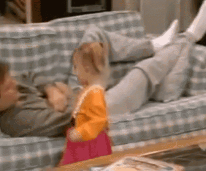 a man is laying on a couch with his feet up and a little girl is standing in front of him .