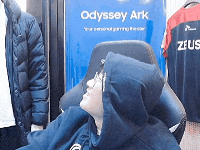 a man in a hoodie is sitting in front of a sign that says odyssey ark