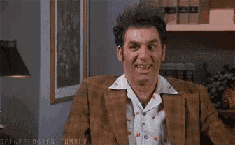 a man in a brown suit and white shirt is sitting in a chair with his mouth open and making a funny face .