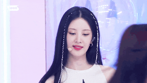 a young woman with long black hair is wearing a white tank top and a microphone .