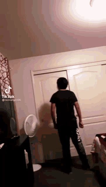 a man in a black shirt is standing in a room with a fan .