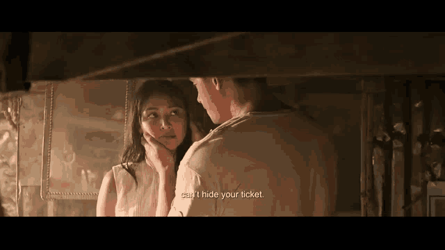 a man and a woman are looking at each other in a room and the woman is touching the man 's face .