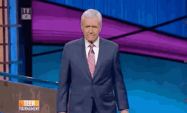 a man in a suit and tie stands in front of a tv screen that says teen tournament on it
