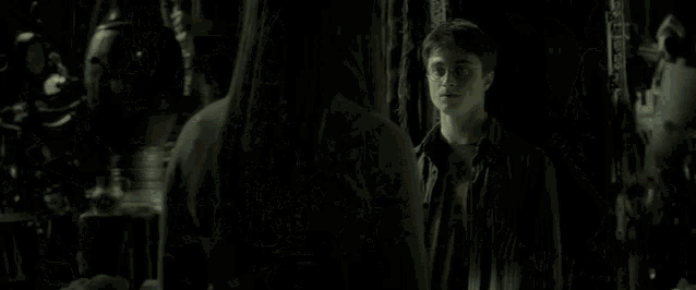 a young man wearing glasses stands in a dark room .