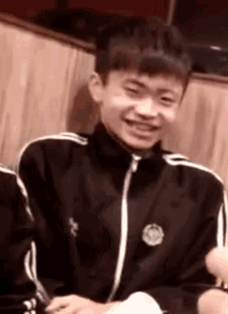 a young boy in a black jacket is smiling while sitting at a table in a restaurant .