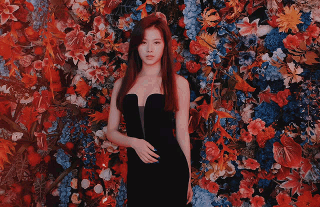 a woman in a black strapless dress is standing in front of a wall of flowers